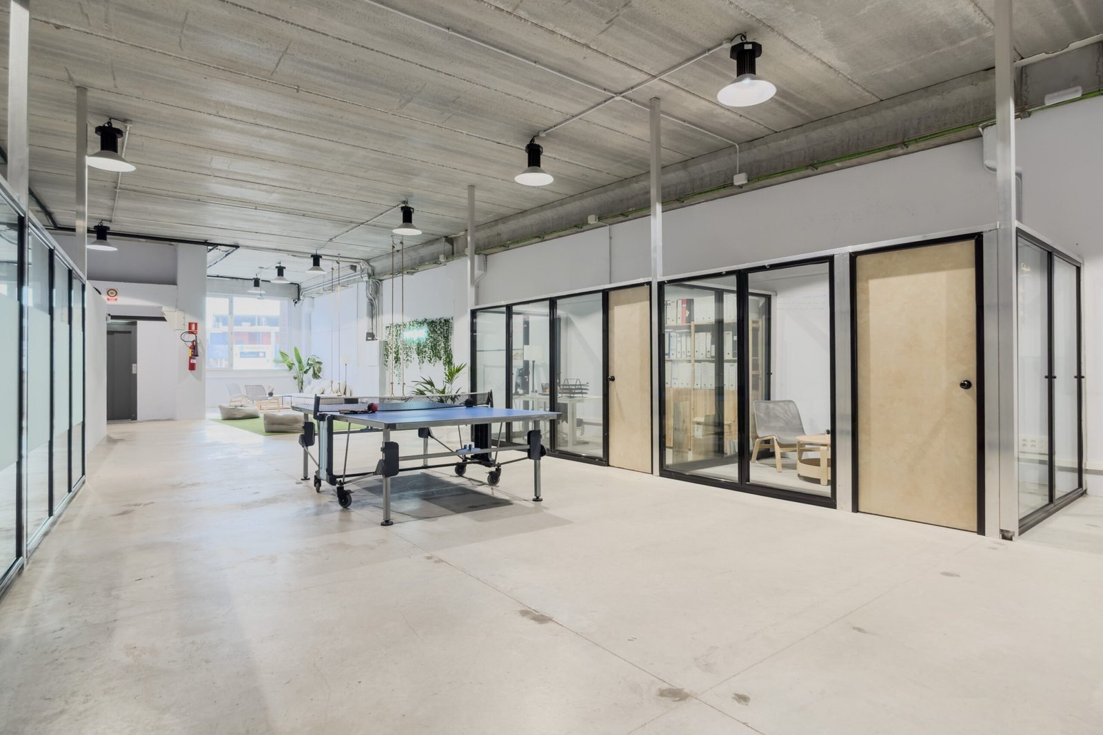Pasillo de la nave con la mesa de ping-pong y los despachos acristalados; al fondo, la zona verde.